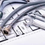 Close-up of plumbing tools and faucet on top of an architectural blueprint, perfect for hardware and construction themes.